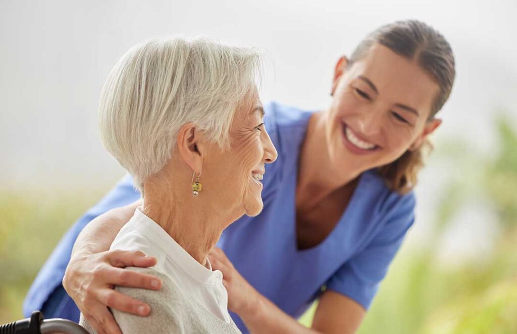 Older adults share a meal in a bright assisted living dining room while a caregiver offers support.